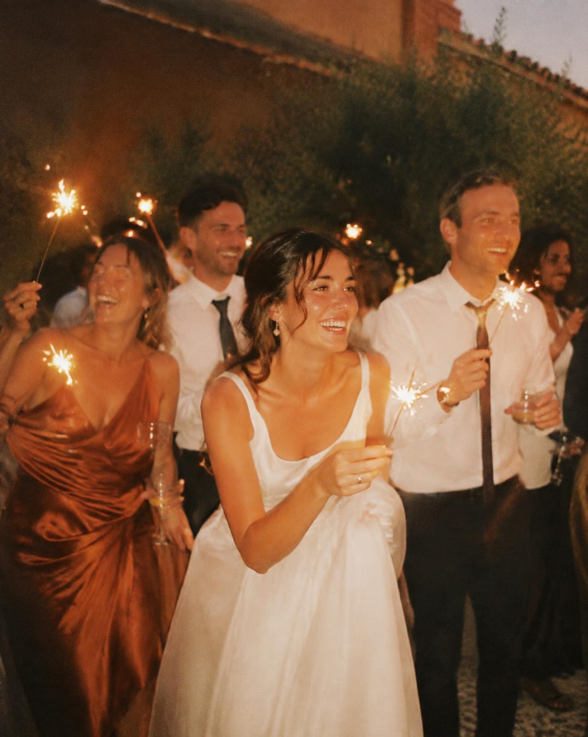 Wedding guests laughing with sparklers at dusk